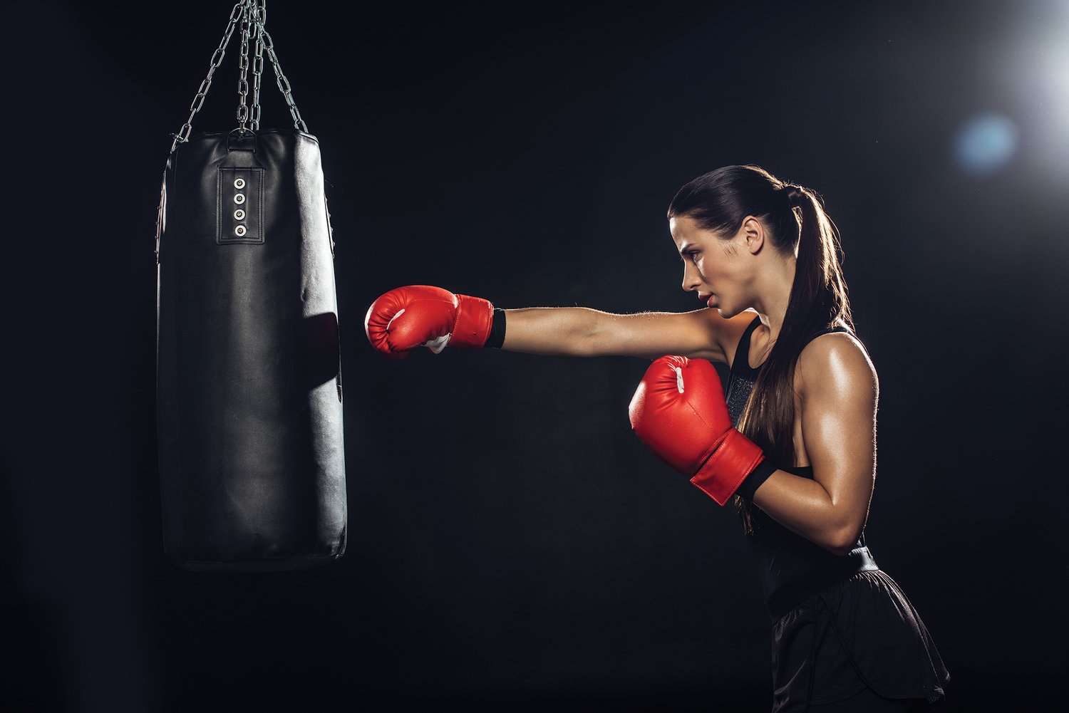Side view of a female boxer in red boxing gloves training with the punching bag